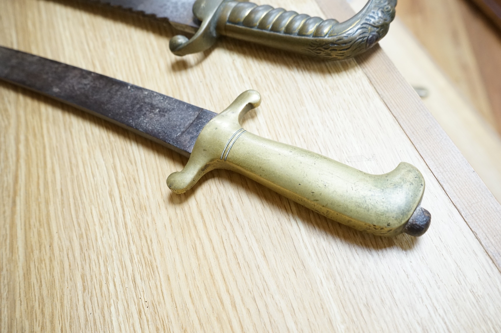 A British Pioneer’s sidearm with brass stirrup hilt, lion’s head pommel and sawback blade, together with an Imperial German sidearm with one piece brass hilt and slightly curved single edge blade